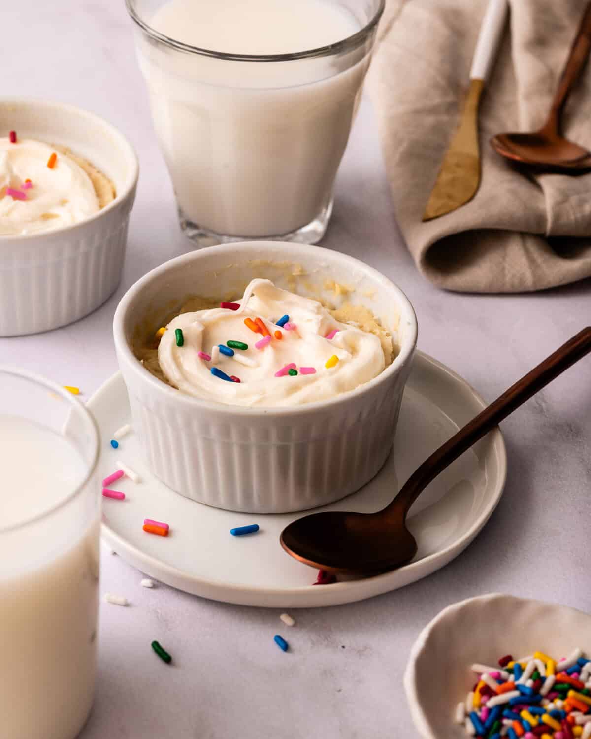 3 ingredient funfetti mug cakes with frosting and sprinkles set on a table with a glass of milk