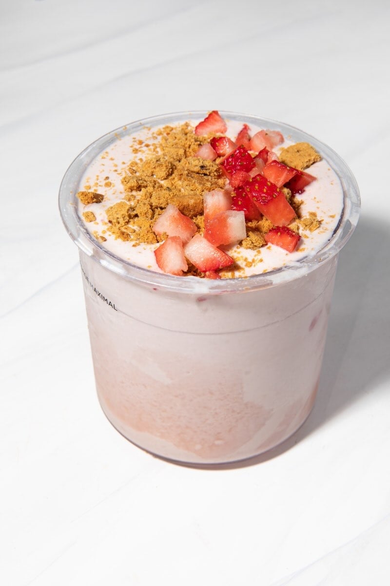 strawberry cheesecake ninja creami in a pint container with strawberry slices and graham crackers on top