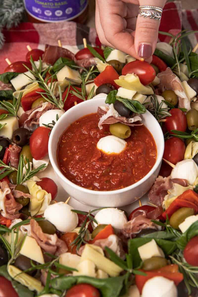 holiday antipasto wreath dipping skewer into sauce bowl