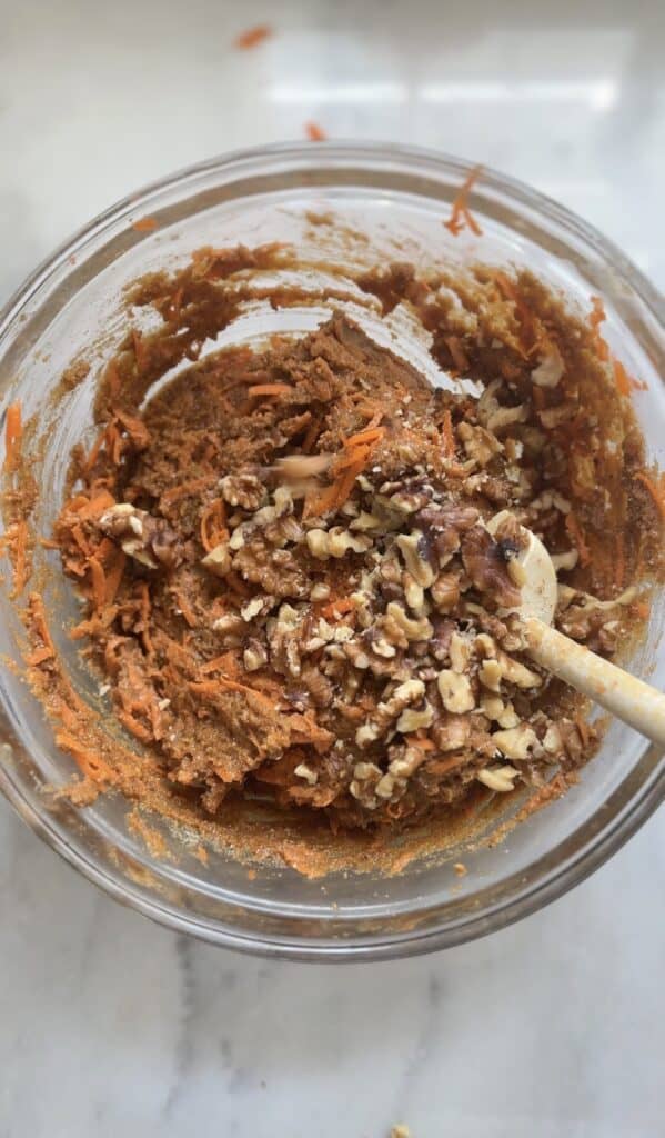 Fold in the shredded carrots and walnuts into the high protein carrot cake batter in a bowl.