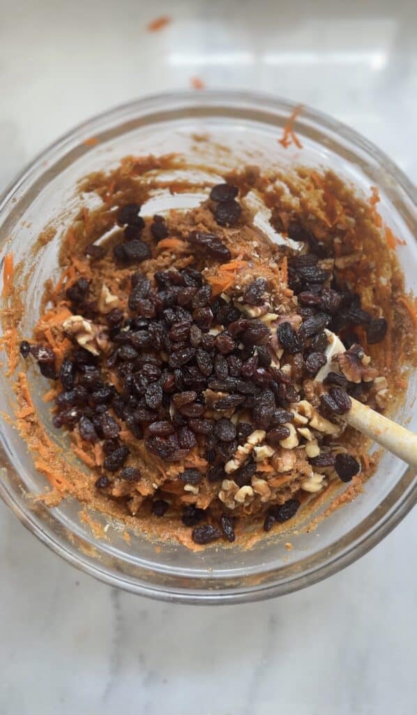 Fold in the shredded carrots, walnuts, and raisins into the high protein carrot cake batter in a bowl.