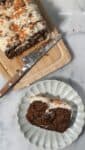 close up of the baked and frosted protein carrot cake on a cutting board and a plate for serving.