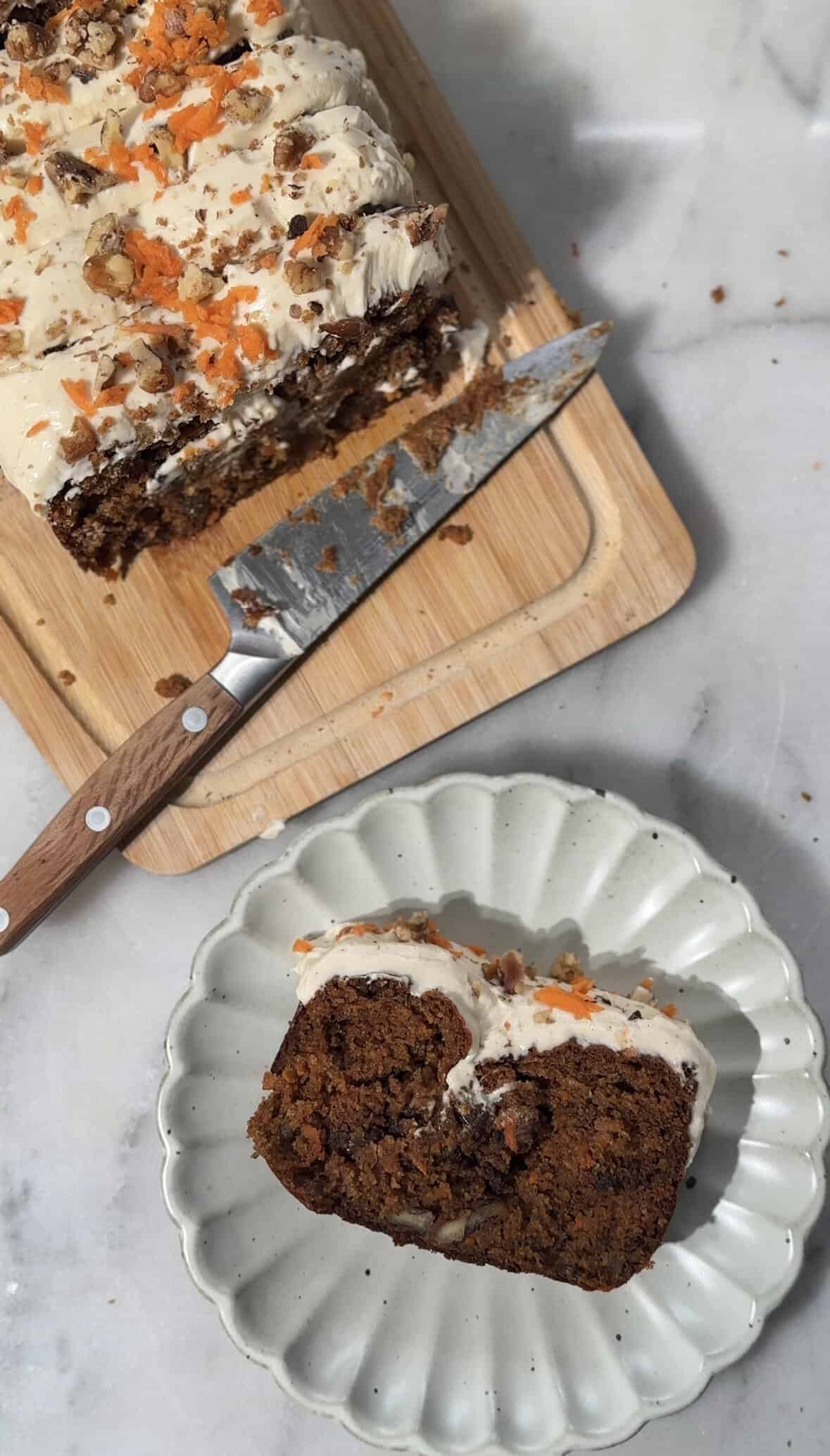 Close up of the baked and frosted Easy High Protein Carrot Cake on a cutting board and a plate for serving.