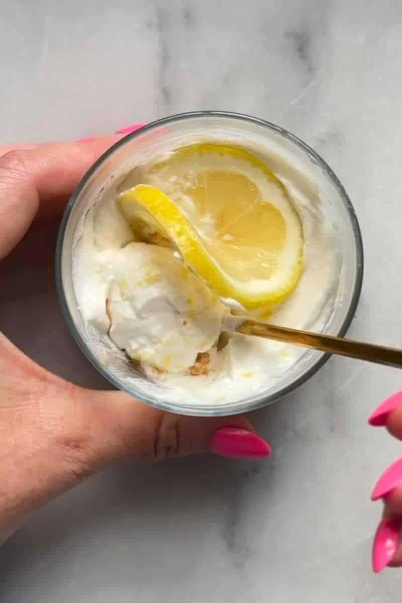 Finished No Bake Lemon Cottage Cheese Cheesecake Cups with fresh lemon garnishes being eaten with a spoon.