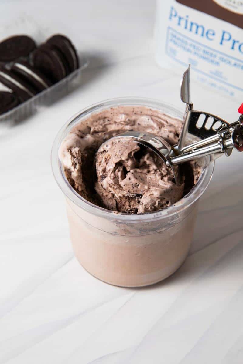 Completed Ninja Creami Protein Dairy Free Oreo Cookies and Cream Ice Cream in the Ninja Creami pint with crushed up gluten free Oreos being scooped with an ice cream scoop.