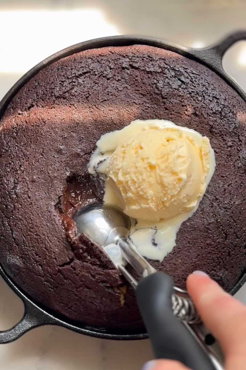 scooping a protein skillet brownie with ice cream on top.