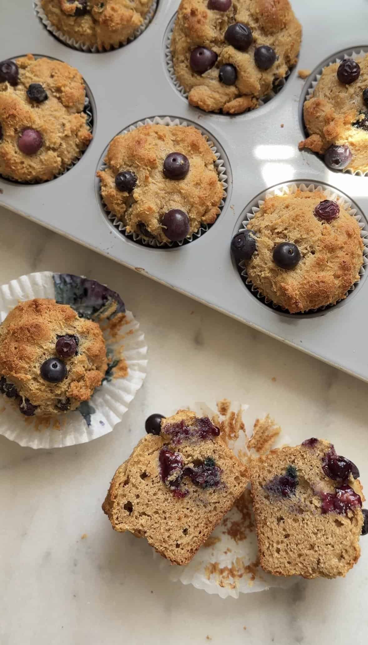 Finished Gluten Free Blueberry Cottage Cheese Protein Muffins inside and outside of the muffin tin, one cut open to see the inside of the muffin.