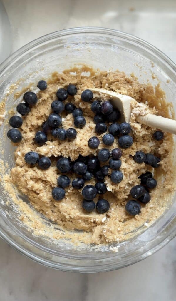 Fold in the blueberries into the combined dry and wet ingredients of the blueberry cottage cheese protein muffins in a bowl with a silicone spatula.