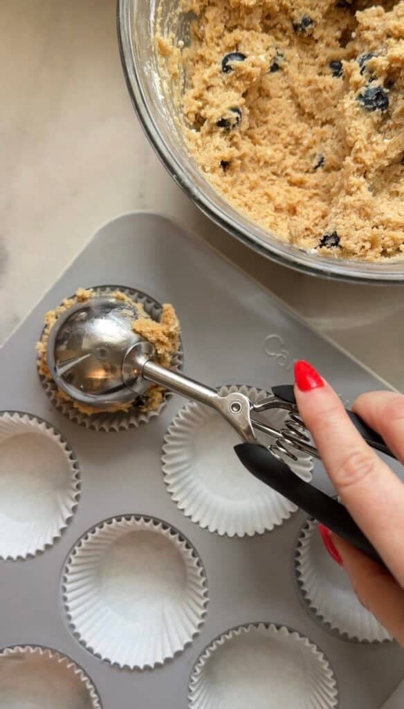 Scoop the blueberry cottage cheese protein muffin batter with a scoop into the parchment lined muffin tin to be baked.