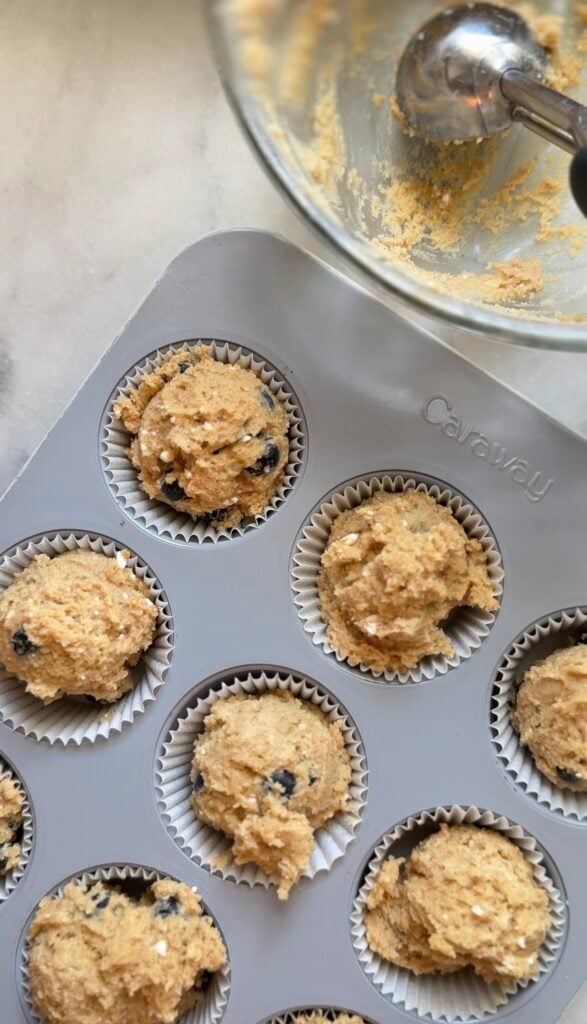Picture of the scooped blueberry cottage cheese protein muffin batter in the parchment lined muffin tin to be baked.