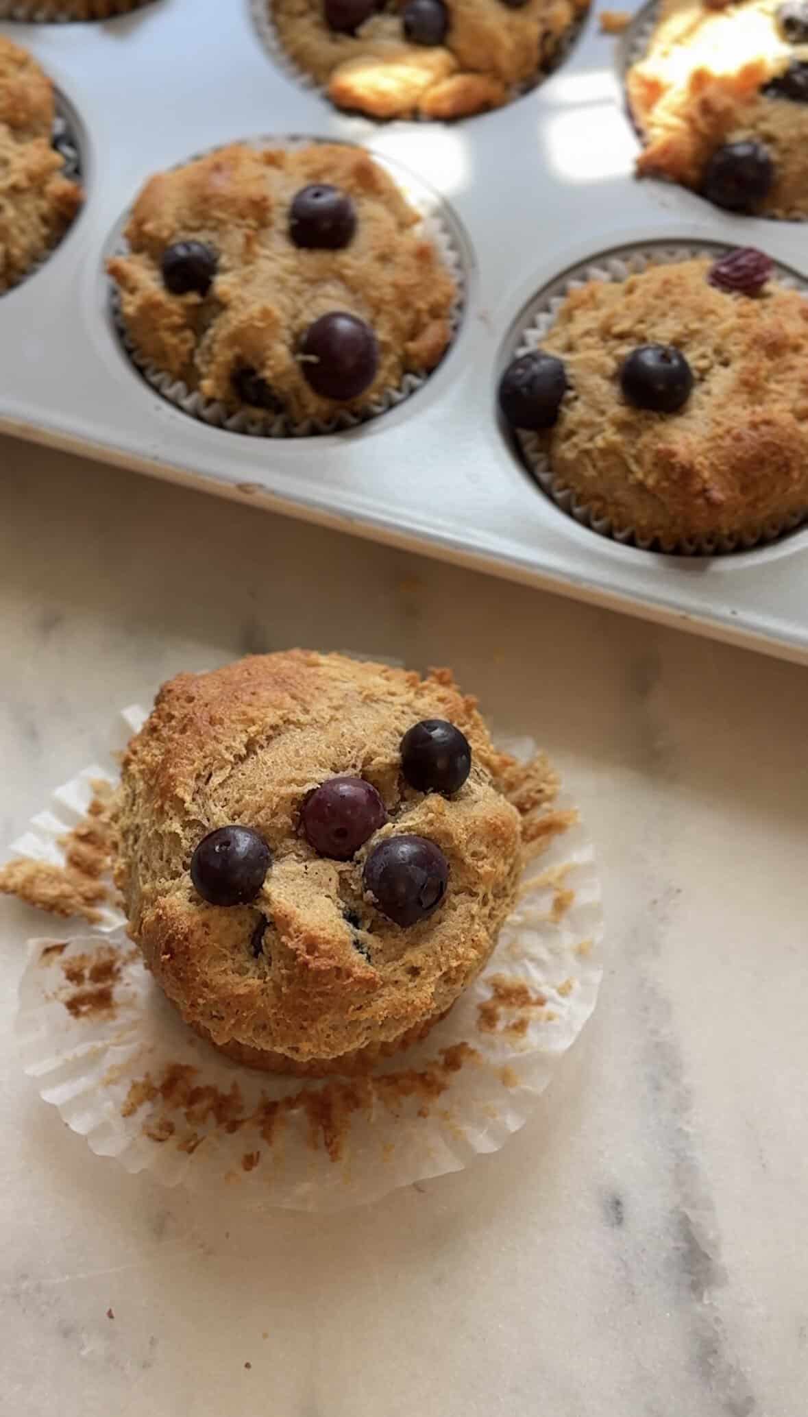 Close up to the finished Gluten Free Blueberry Cottage Cheese Protein Muffins, one being unwrapped on the counter.