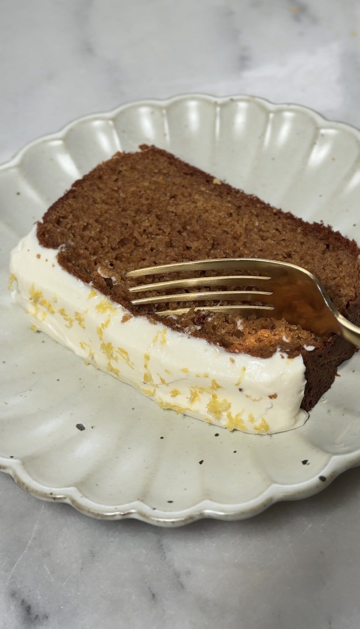 Finished slice of protein lemon cake with protein cream cheese frosting on a plate with a bite almost being taken out.