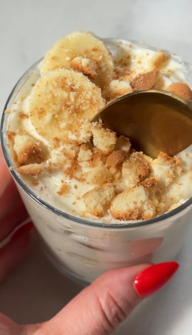 Finished easy protein banana pudding topped with gluten free vanilla wafers and thinly sliced fresh banana being eaten with a spoon.