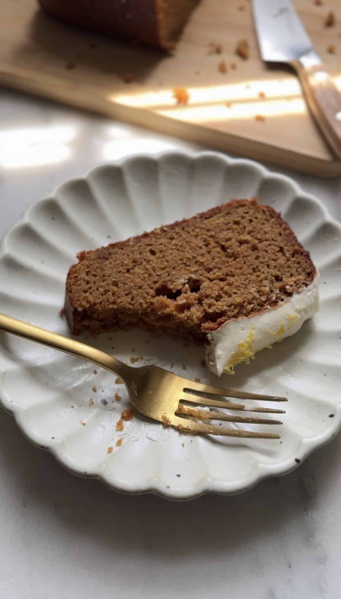 Finished slice of protein lemon cake with protein cream cheese frosting with a bite taken out of it, on a plate and fork.