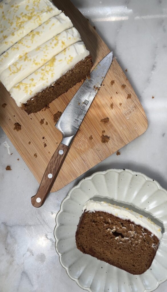Finished cake loaf and slice of protein lemon cake with protein cream cheese frosting on a plate.
