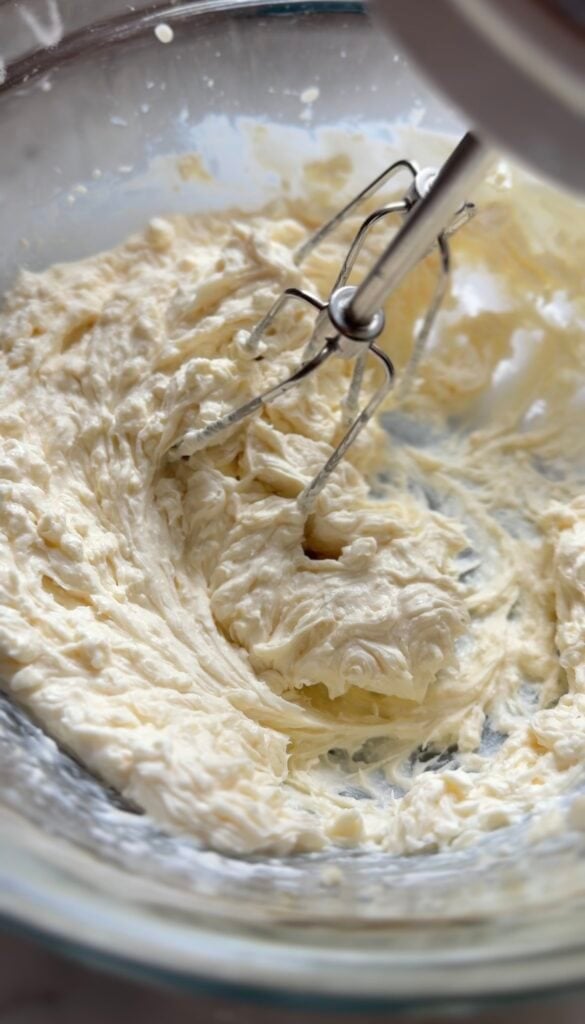 Mixing the protein cream cheese frosting ingredients in a bowl for the protein lemon cake with a hand mixer whisk.