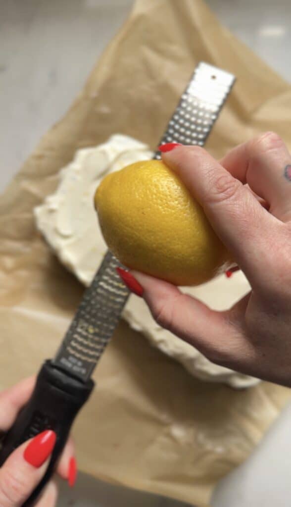 Zesting the lemon zest on top of the protein cream cheese frosting ingredients on top of the protein lemon cake.