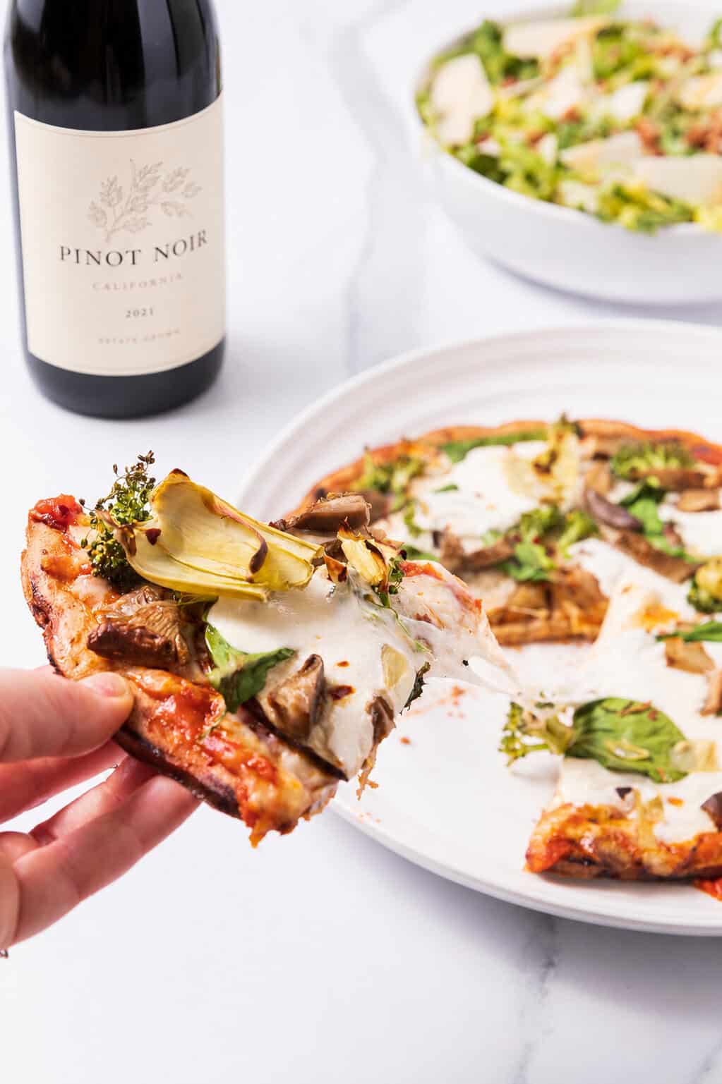 Slice of the roasted veggie pizza slice served with red wine.