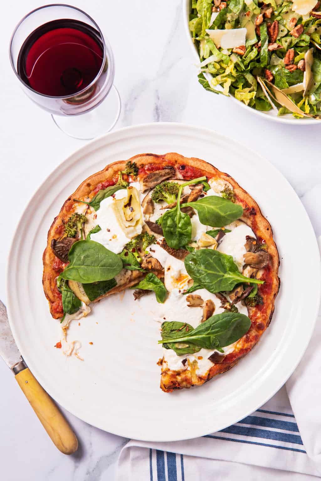 Roasted veggie pizza with a slice out of it, served with a glass of red wine.