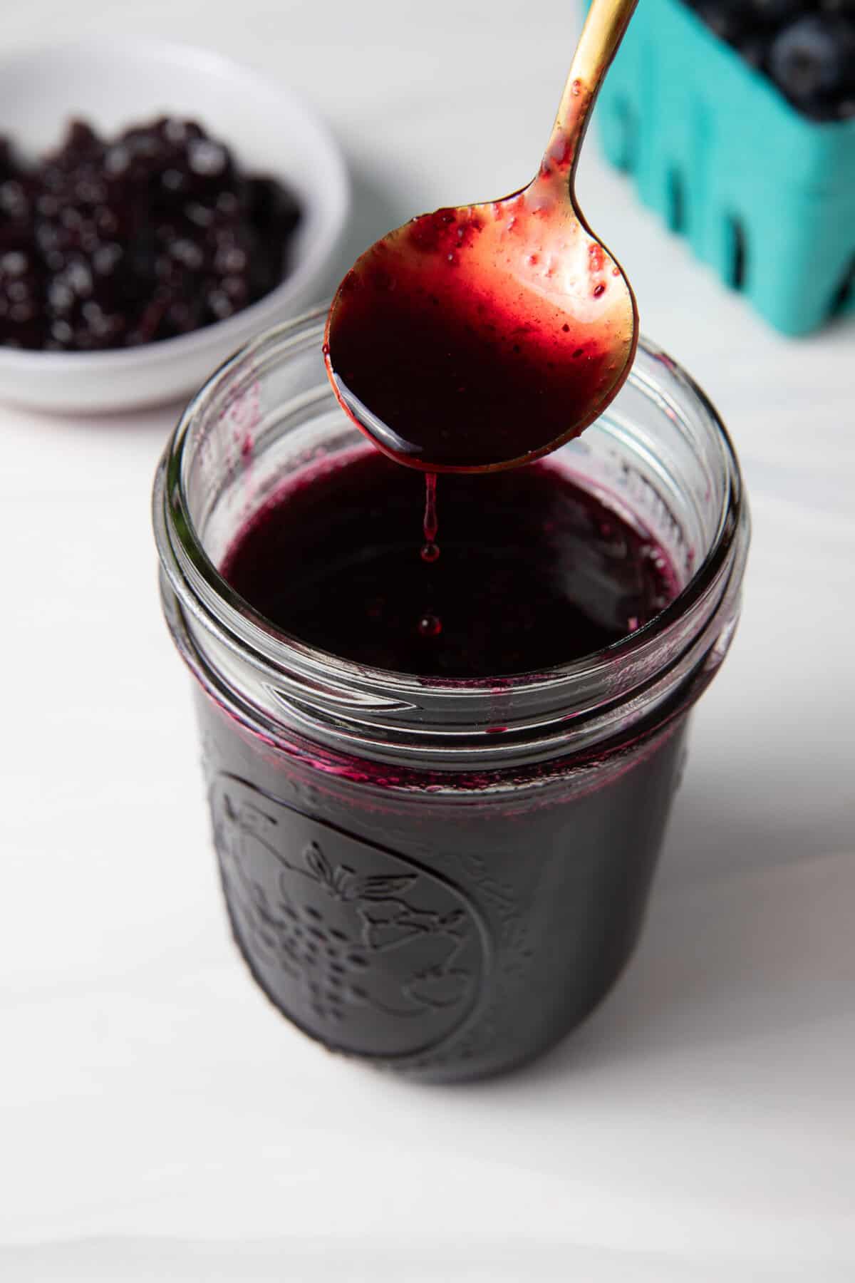Fresh Blueberry Simple Syrup in a jar being spooned to show the syrup texture.