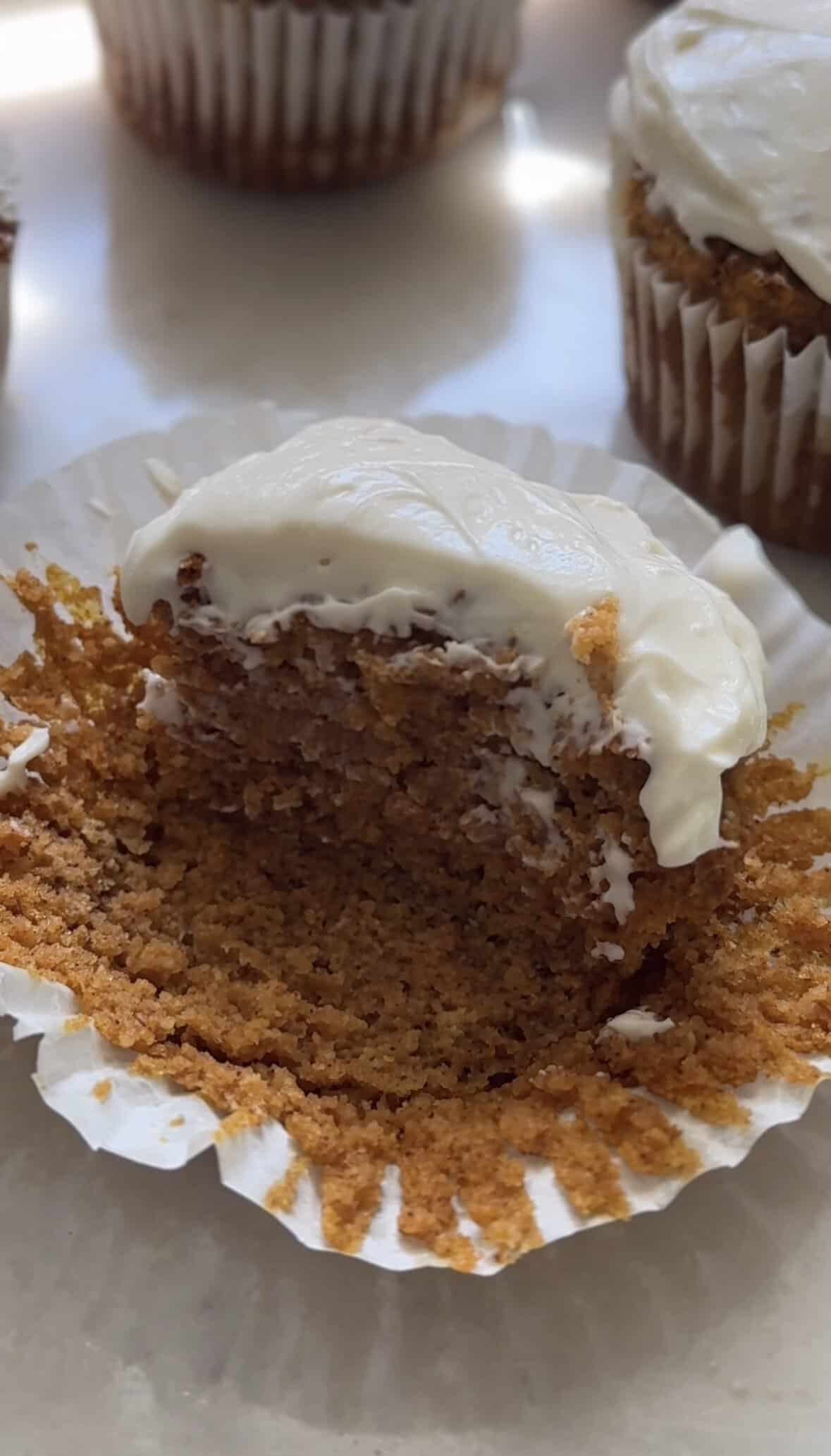 Pumpkin cottage cheese muffins with cream cheese frosting in the muffin liner, half eaten to show texture on the inside.