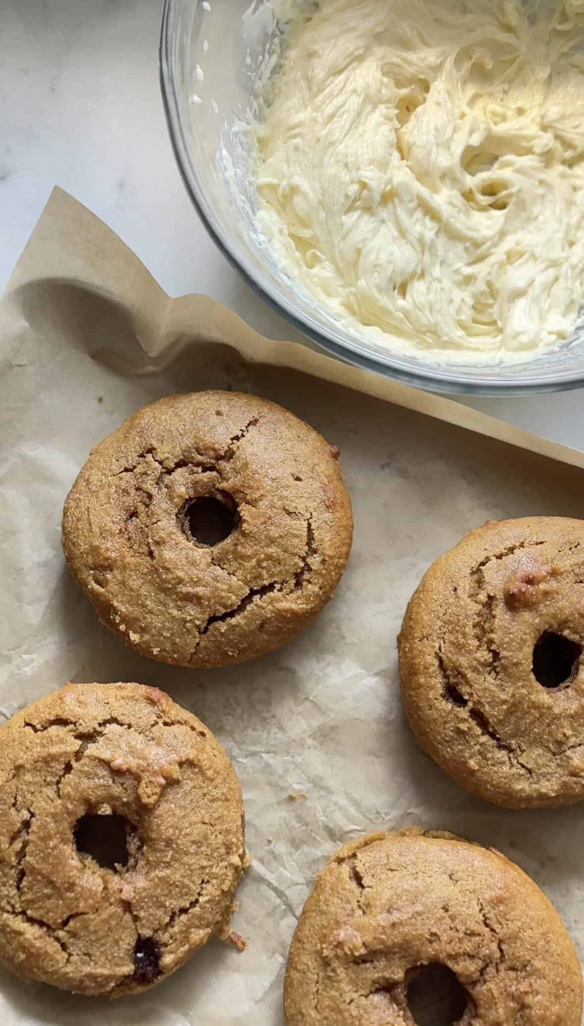 Unfrosted Gluten Free Baked Banana Donuts with the bowl of frosting on the side.