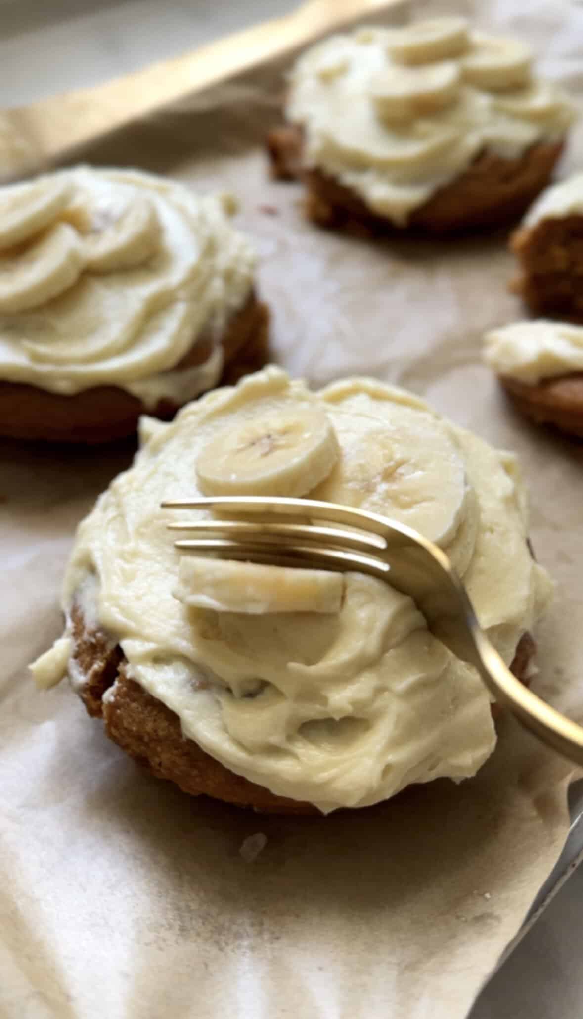 Gluten Free Baked Banana Donuts topped with fresh sliced bananas about to be cut and eaten with a fork.