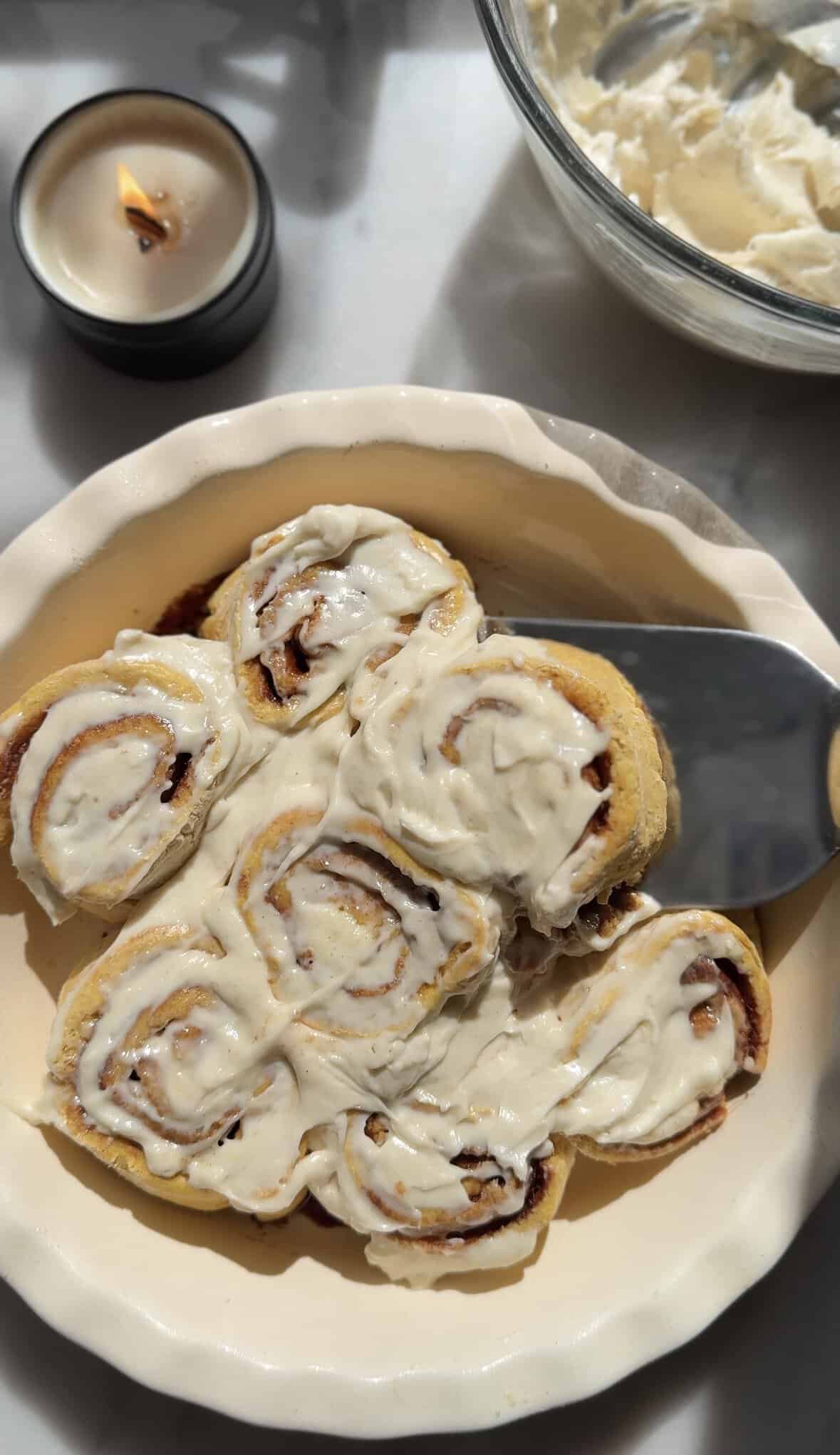 Glazed pumpkin cottage cheese cinnamon rolls in the baking dish with a spatula getting one of the rolls out.