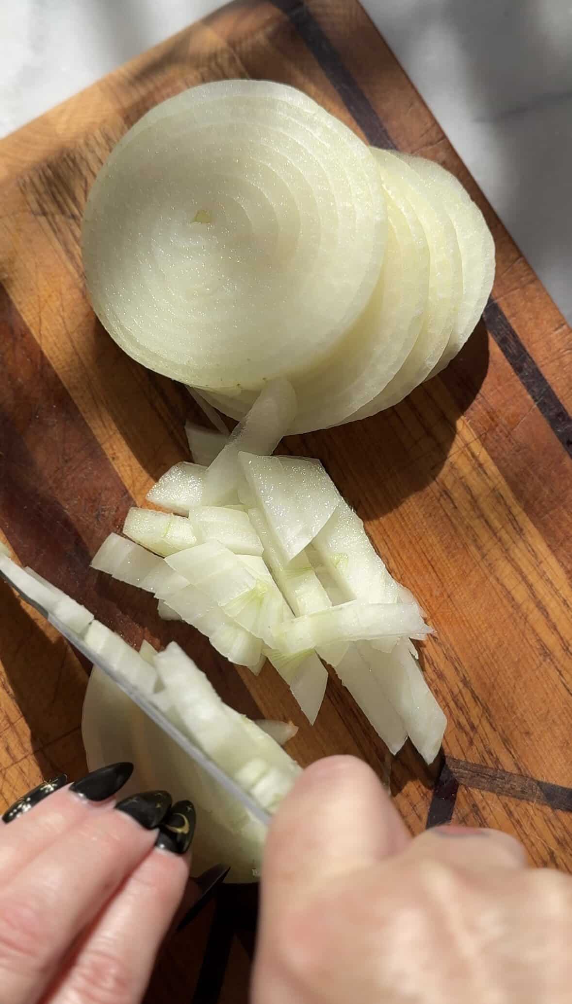 Slice a yellow onion on a cutting board with a sharp knife.