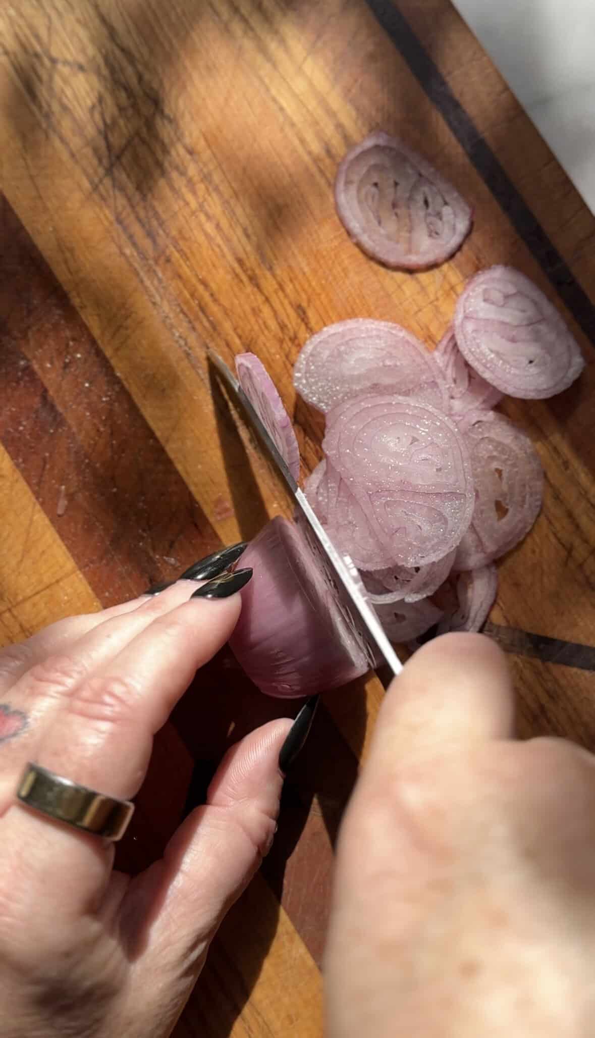 Slice a shallot on a cutting board with a sharp knife.