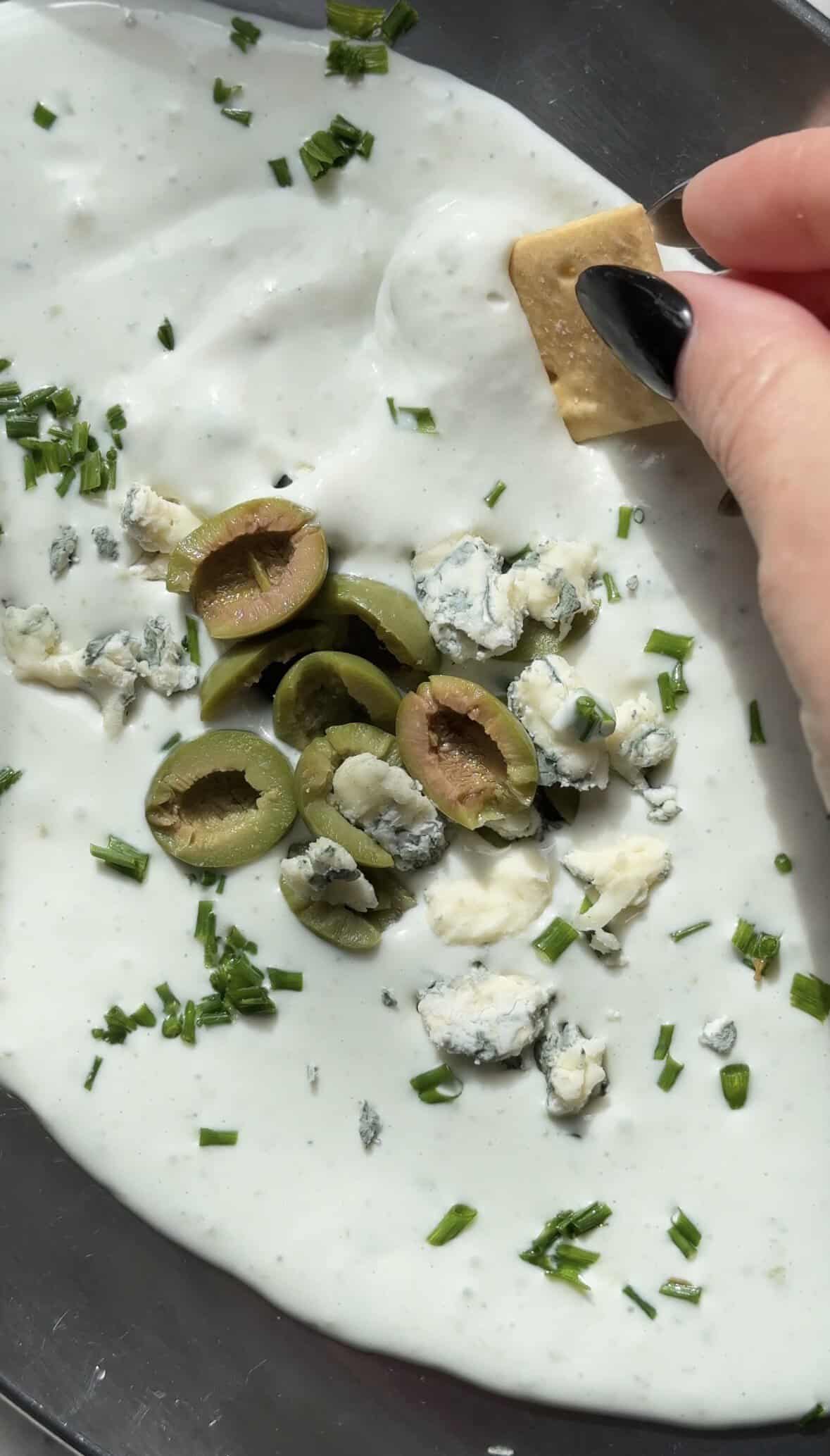 Close of dipping the cracker into the Protein Dirty Martini Dip.