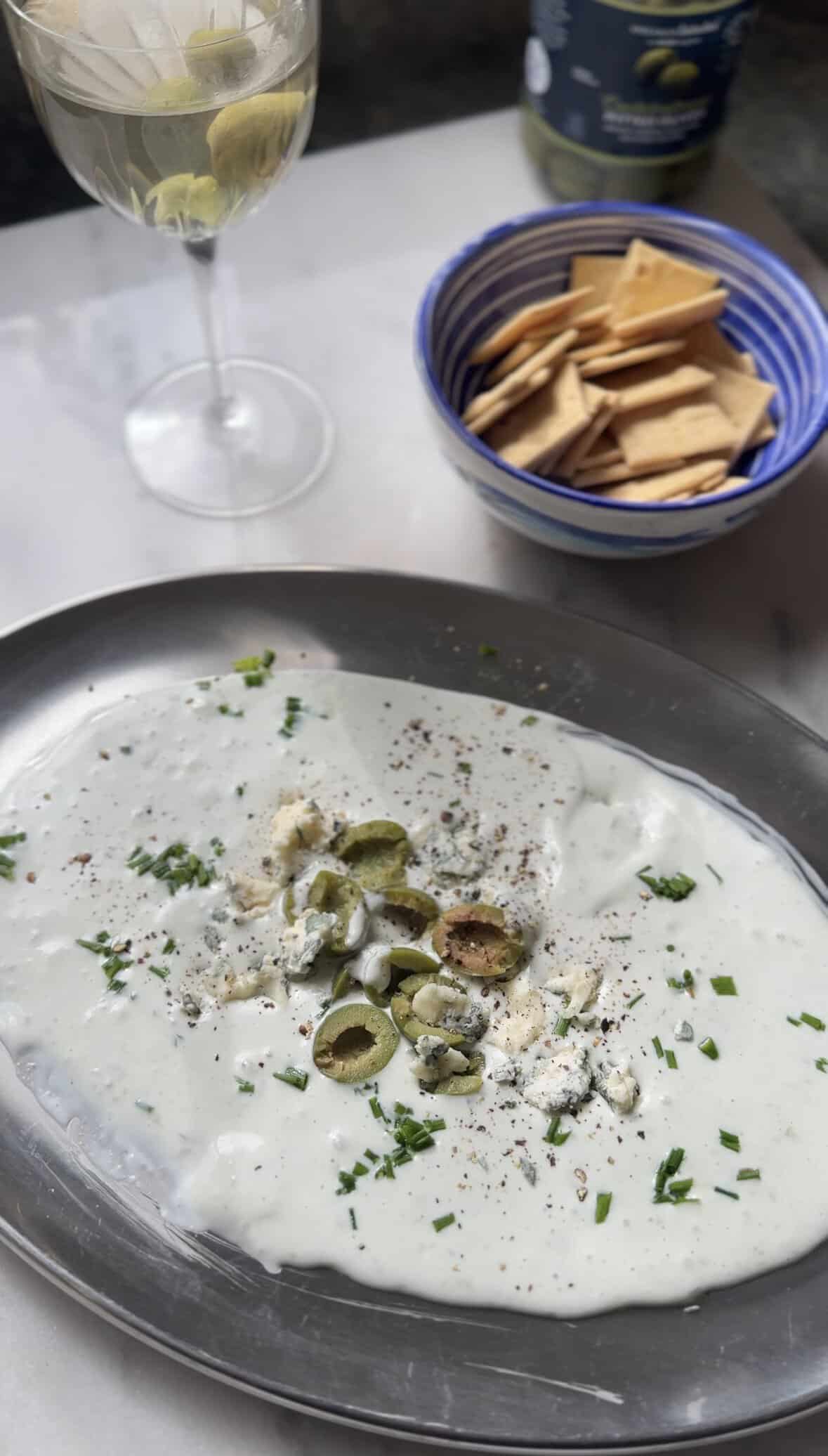 Protein Dirty Martini Dip in a serving bowl served with an actual martini in a glass and crackers.