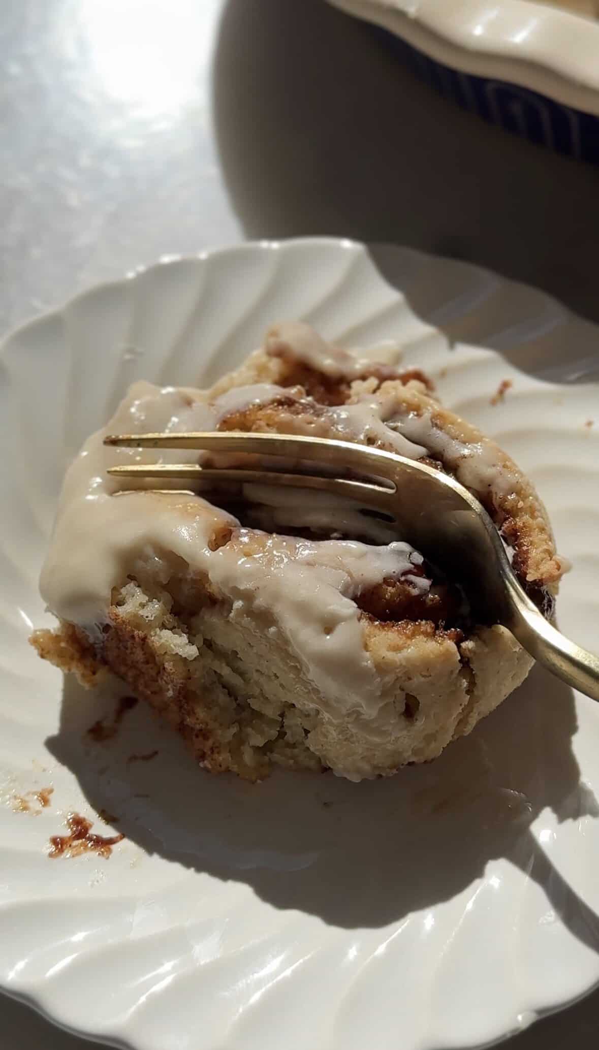 Taking a bite with a fork of the gluten-free cinnamon roll on a plate.