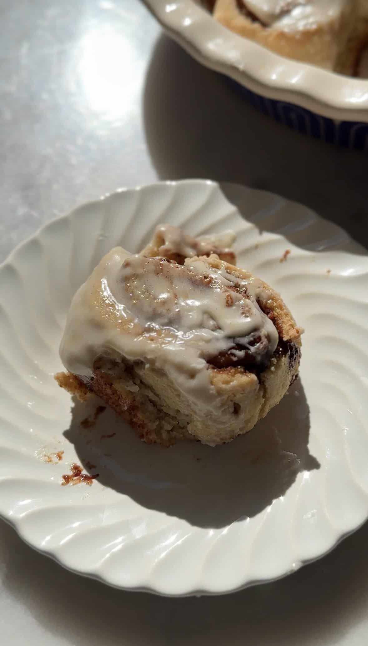 Finished gluten-free cinnamon roll on a plate with cream cheese frosting on top.