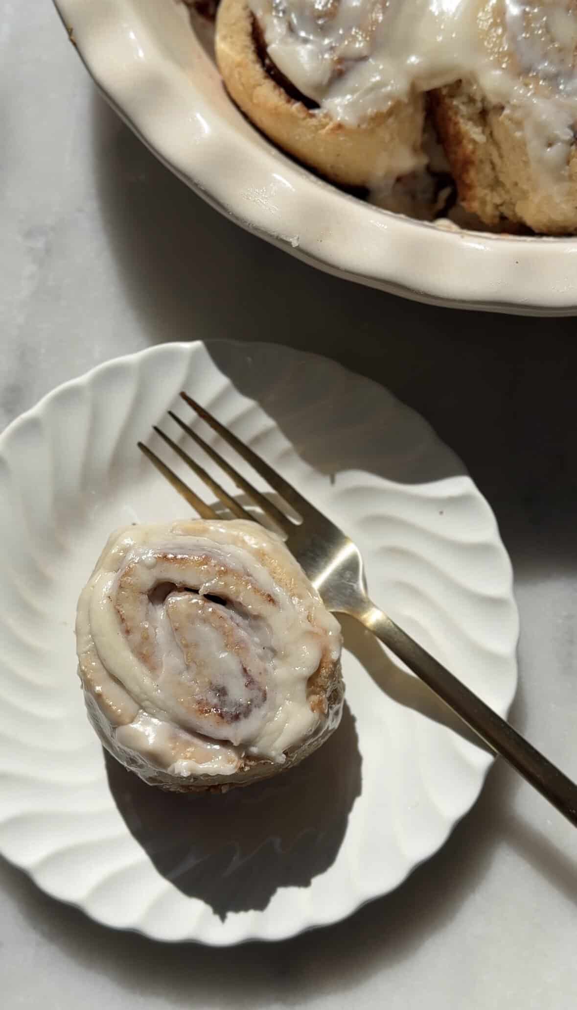 Baked gluten-free cinnamon rolls with cream cheese frosting on a plate with a fork.