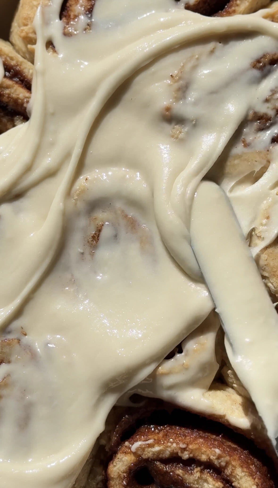 Close up of the cream cheese frosting being frosted on the gluten-free cinnamon rolls.