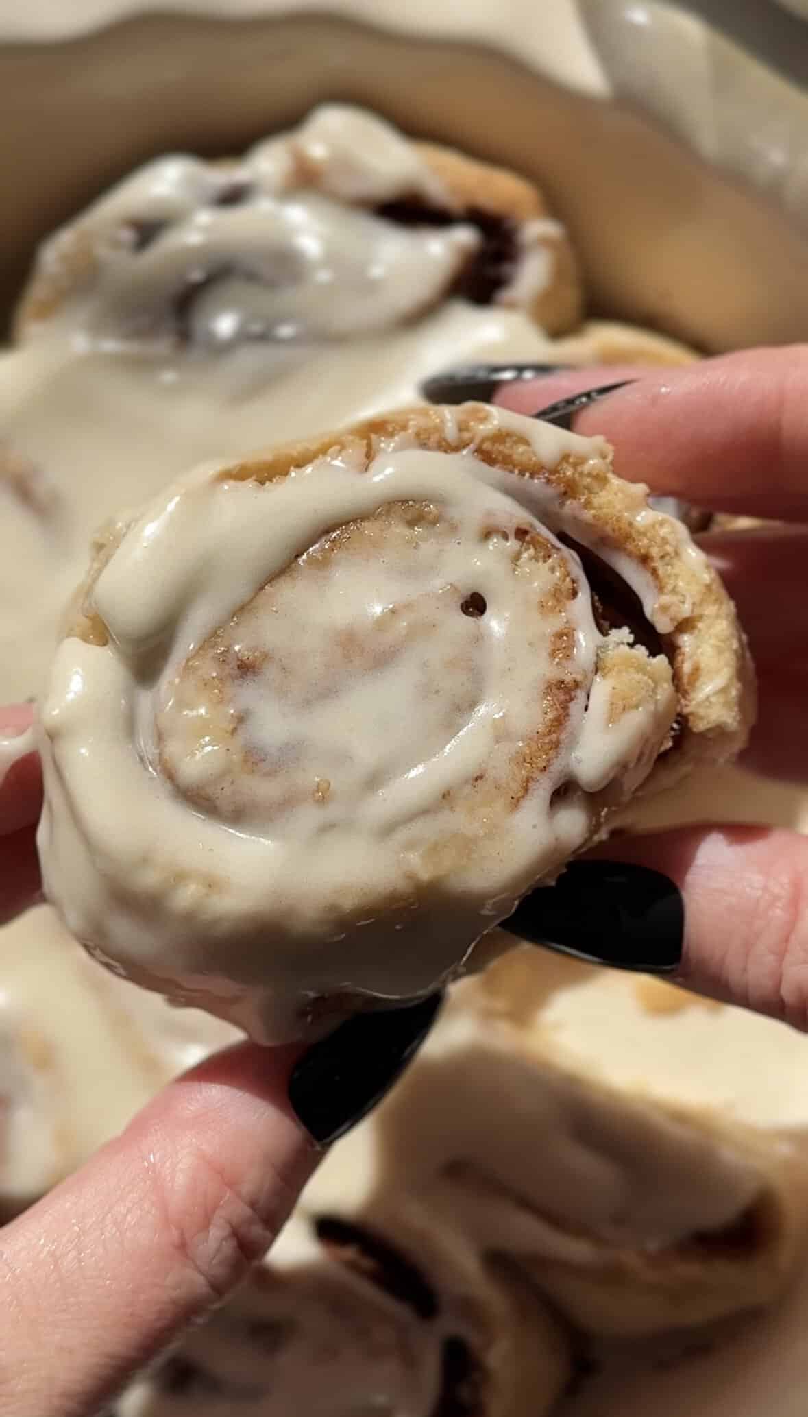 Holding a gluten-free cinnamon roll with my hand to show the top and texture of the cinnamon roll.